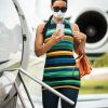 A famous woman with a face mask and sunglasses entering a private plane while holding a mobile phone.